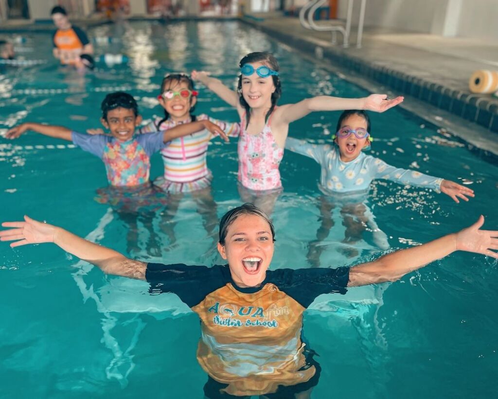 A group of children in the pool with their arms out.